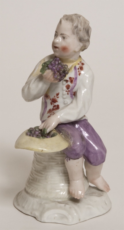 Figurin, gosse sittande på en upp- och nedvänd korg